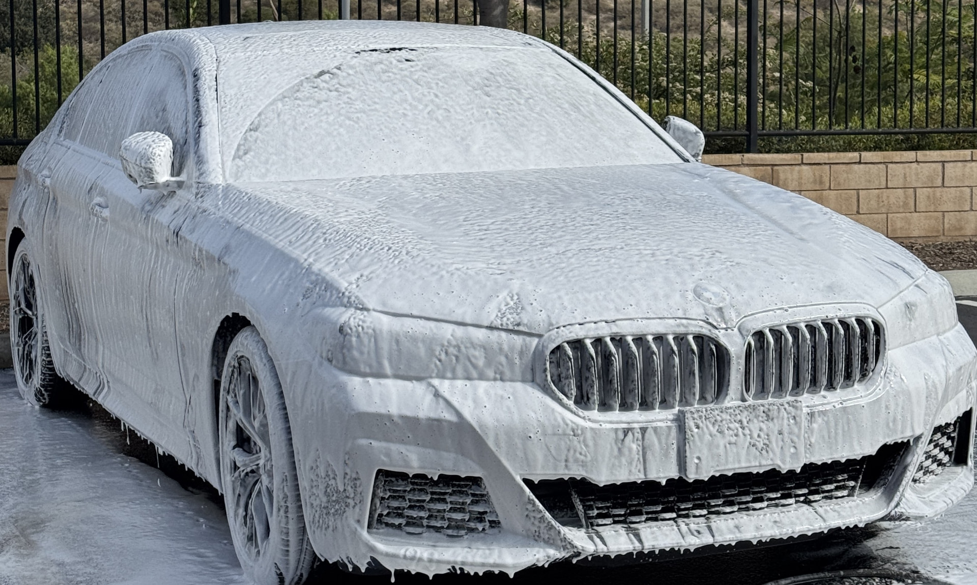 BMW sedan covered in pre-wash foam during a contact wash